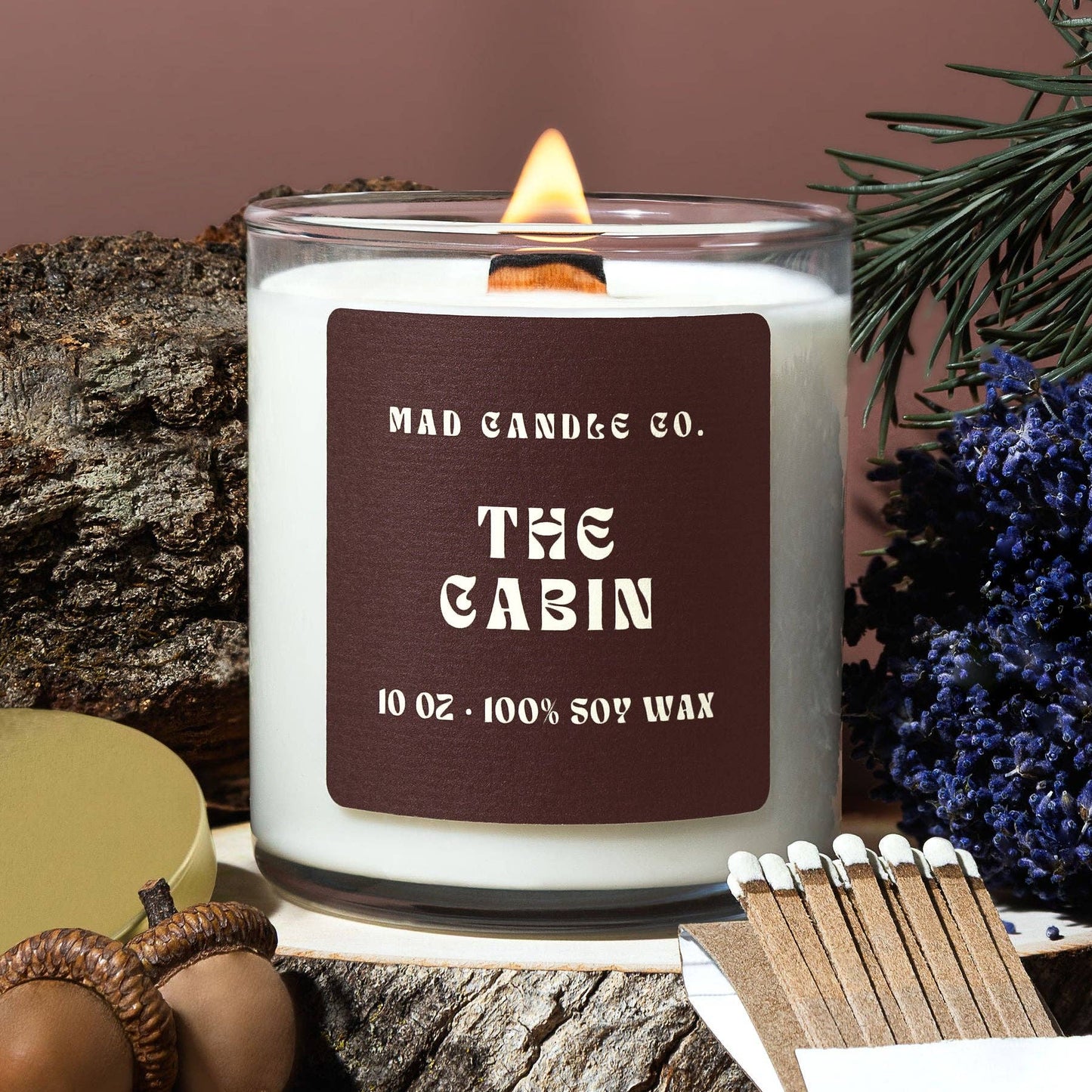 Candle labeled 'The Cabin' from Mad Candle Co. on a wooden surface with decorative elements.